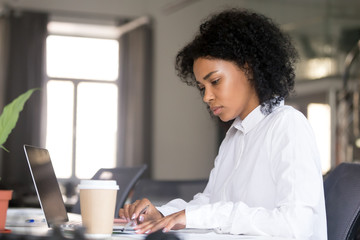 Serious African American woman working with documents at workplace, checking bills, financial reports, making notes with pen in hand, focused female student writing research work, preparing for exam - obrazy, fototapety, plakaty