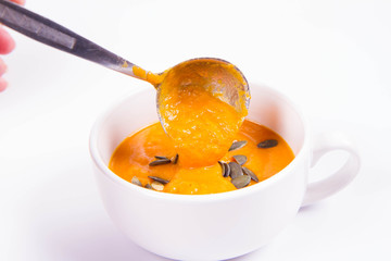 Pumpkin soup decorated with pumpkin seeds being poured into a bowl on a wooden background