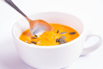 Pumpkin soup decorated with pumpkin seeds being eaten with a spoon on a white background