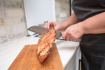female cook cuts smoked pork ribs on a wooden cutting board in the kitchen. Non vegan food