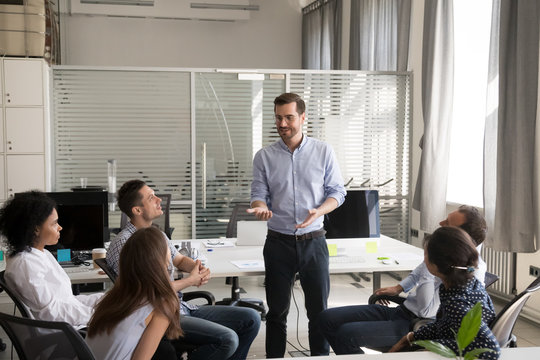 Confident male leader, coach holding briefing for multiracial team employees in office, discussing, explaining business strategy, plan to subordinates, businessman at company meeting with colleagues