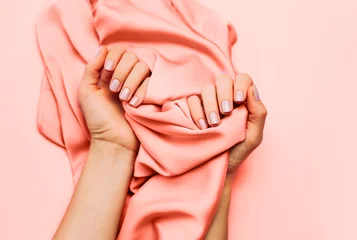 Schöne Frauenmaniküre auf kreativem Living Coral-Hintergrund mit Seidenstoff. Farbkonzept des Jahres 2019. Ansicht von oben, flach gelegt. Kopieren Sie Platz für Ihren Text. © paninastock