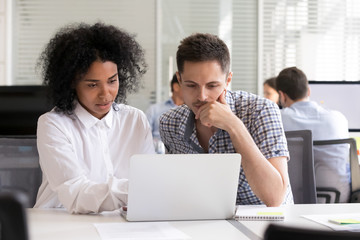 Serious diverse office colleagues discussing online project results, using laptop at workplace,...