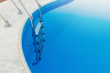Close-up of a part of swimming pool with a stainless steel ladder and blue water on sunset. Summer vacation, holidays, relax, summer activities concept