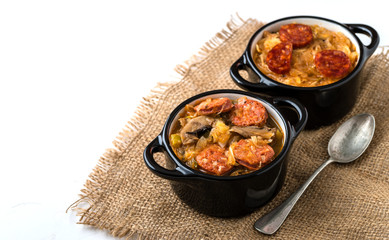 Slovak Christmas national cabbage soup in two small black pots with sausage on the tablecloth background.