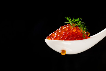 Portion of red caviar with dill in a ceramic white spoon on a black background