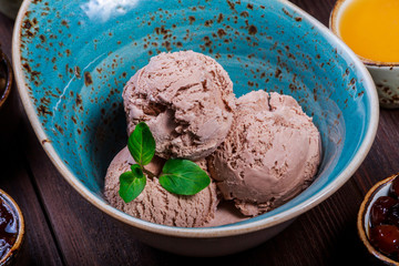 Chocolate ice cream scoops in bowl with mint leaves on wooden background
