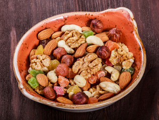 Nuts mix in a bowl on dark wooden background. Walnuts, pistachios, almonds, hazelnuts, cashews and dried fruits mix. Healthy food and snack