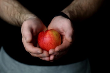 Male hands holds and gives a fresh juicy red apple, offering healthy nutrition food and diet, on a black background
