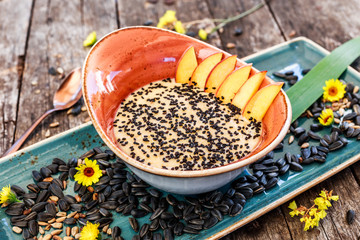 Oatmeal porridge with sunflower seeds, sesame and peaches on bright wooden table. Selective focus. Healthy breakfast, vegan food
