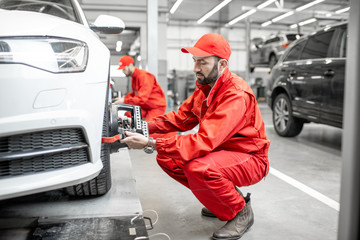Two auto mechanics in red uniform fixing disk for wheel alignment on a luxury car at the car service