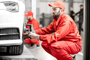 Two auto mechanics in red uniform fixing disk for wheel alignment on a luxury car at the car service