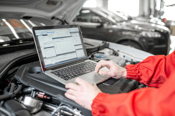 Auto mechanic diagnosing car engine with a laptop with special program, close-up view with no face