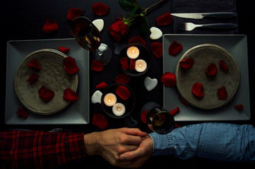Handsome young gay couple having romantic diner holding hands. Top view. Candles, flowers and wine