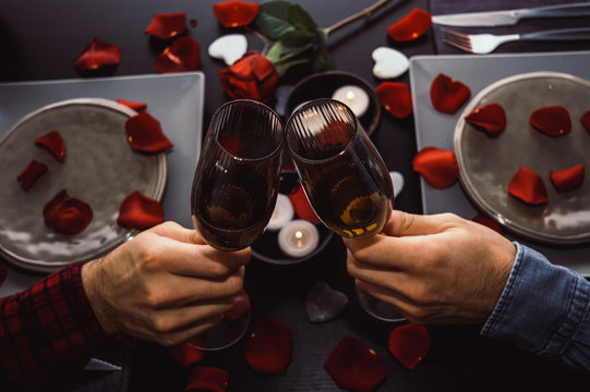 Happy Young Gay Couple Toasting Champagne Glasses Having Romantic Dinner. Top View. Candles, Flowers And Wine