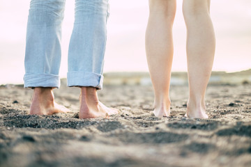ground and rear view of feet from man and woman couple in friendship or relationship - naked nude young bodies enjoying the sand at the beach - naturism concept for alternative vacation