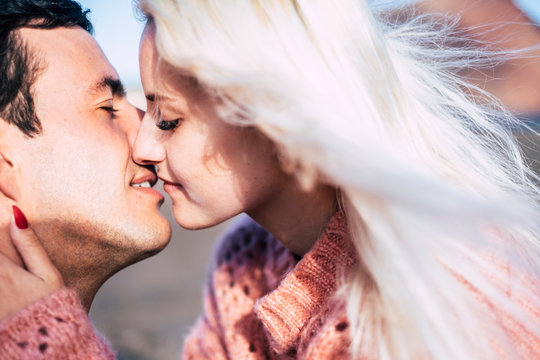 closeup portrait of young beautiful attractive caucasian couple kissing under the sun in outdoor space - love and kiss young people millennial concept - bright image and romantic feeling
