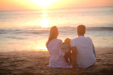 parents with a child sit on the beach and watch the sunset