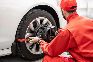 Handsome auto mechanic in red uniform fixing disk for wheel alignment at the car service