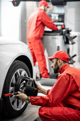 Fototapeta na wymiar Handsome auto mechanic in red uniform fixing disk for wheel alignment at the car service