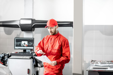 Auto mechanic in red uniform working with computer doing wheel allignment at the car service