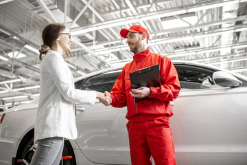 Young woman client shaking hands with auto mechanic in red uniform having a deal at the car service