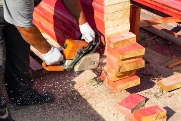 A worker saws off a chainsaw wood Board. House construction. - obrazy, fototapety, plakaty