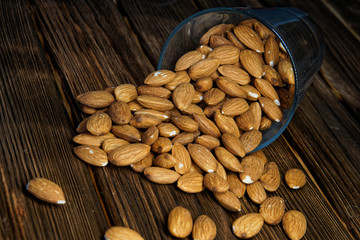 Almond nuts in a tipped glass on a wooden background