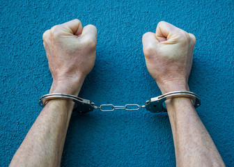 Caucasian male hands in handcuffs against a blue background