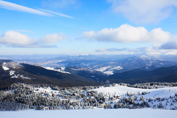 Fototapeta na wymiar Panoramic view of Dragobrat ski resort from above. Mountain winter snowy landscape from ski slope. Wooden cottages and hotels in valley. Empty slope, no people. Product placement background for design