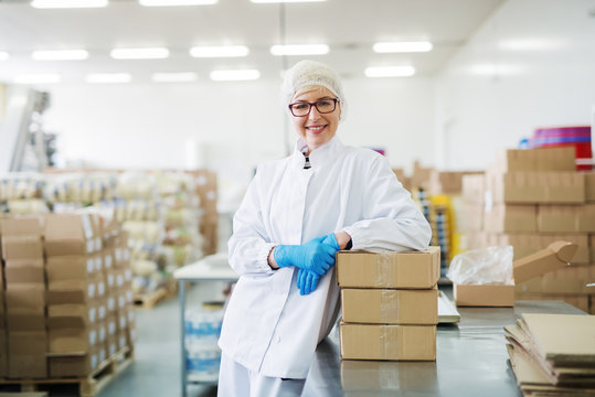 Smiling female worker leaning on boxes. Warehouse interior.