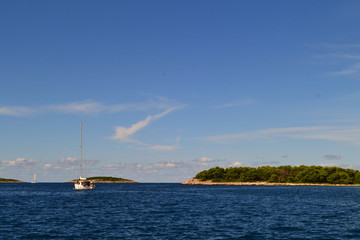 Green islands in the azure sea. A boat in the distance and blue sky. Croatia.