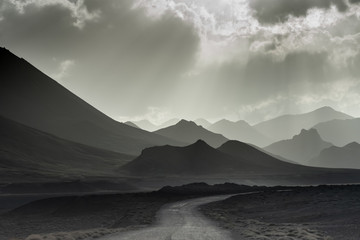 Fototapeta premium Monochrome landscape of layered mountains. Silhouettes of mountains in the setting sun. Black and white landscape. The road among the rocks.