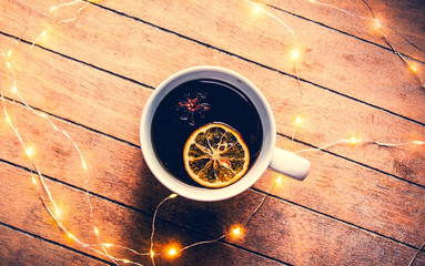 Cup of tea with lemon and star anise with Christmas lights on wooden background