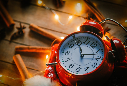Vintage alarm clock and cinnamon, star anise with Christmas lights around on wooden background