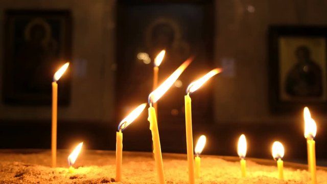Candles are burns and standing in the sand in candlestick in an Orthodox church