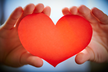 Valentine's Day theme with red paper heart in young woman's hands, close-up