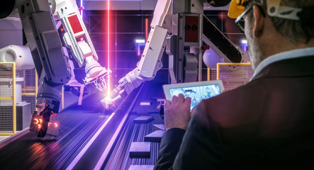 Smart automation industry robot in action welding metall while engineer uses his remote control...