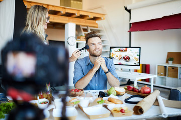 Portrait of make-up artist applying finishing touches to handsome TV show host in cooking studio , copy space