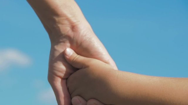 The parent takes the hand of the child. Mother holds the hand of the child against the blue sky.