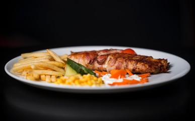 chicken meat with bacon. chicken meat with french fries and corn. fast food meal on black background. 