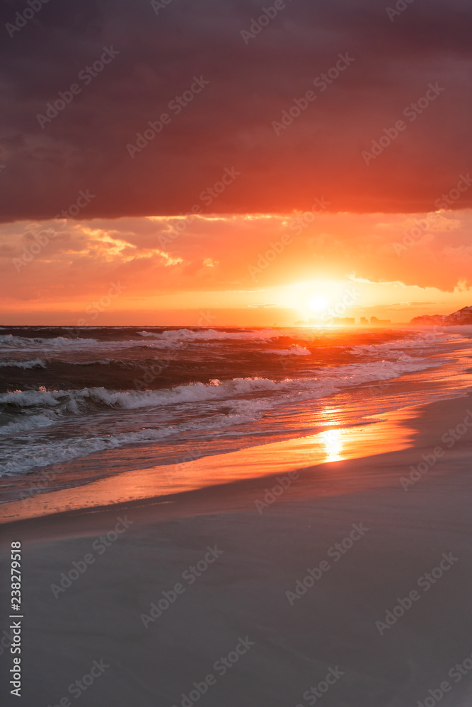 Wall mural Dramatic vertical orange red sunset in Santa Rosa Beach, Florida with Pensacola coastline coast cityscape skyline in panhandle with ocean gulf mexico waves - Wall murals