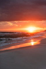 Dramatic vertical orange red sunset in Santa Rosa Beach, Florida with Pensacola coastline coast cityscape skyline in panhandle with ocean gulf mexico waves