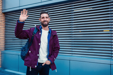 Half length portrait of handsome bearded man dressed in fashionable clothes standing on street.