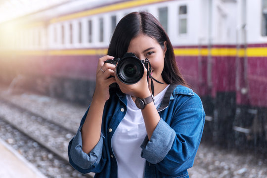 Photographer young woman taking pictures holding digital camera in station. Attractive girl travel with her camera in train station on rainy day.