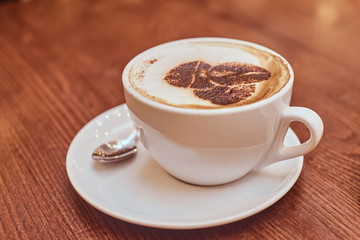 Hot coffee with art in a cup on the wooden table in a coffee shop, blur background with bokeh effect