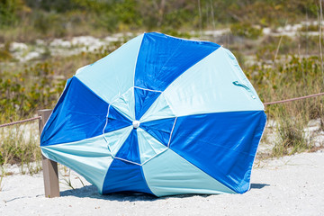Sanibel Island, USA Bowman's beach, Florida with closeup of umbrella on sand, nobody during sunny day, blown away by hurricane storm wind