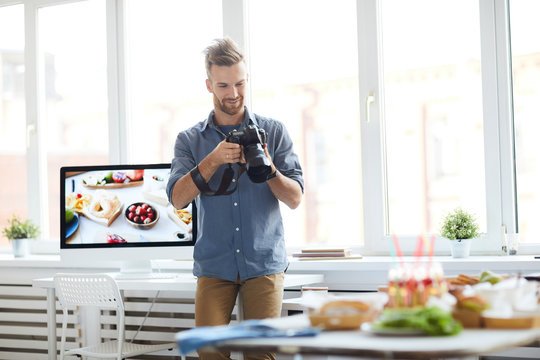 Portrait of successful photographer taking pictures of table with food while working in photo studio, copy space