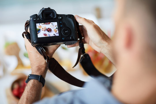Above view closeup of unrecognizable photographer holding professional photo camera while taking pictures of food on table, copy space