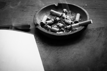 cenicero con colillas y cigarro encendido sobre escritorio